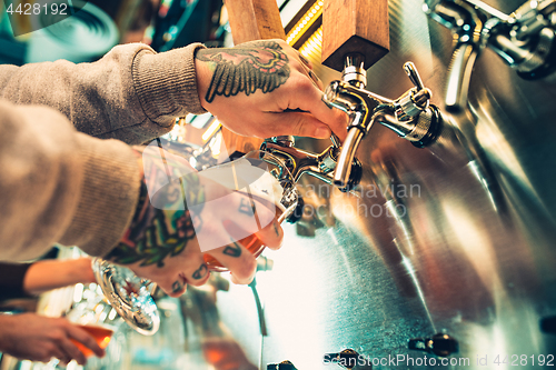 Image of Hand of bartender pouring a large lager beer in tap.