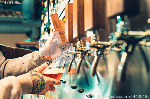 Image of Hand of bartender pouring a large lager beer in tap.