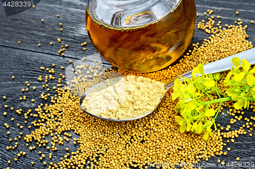 Image of Mustard powder in spoon with oil and flower on black board