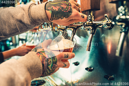 Image of Hand of bartender pouring a large lager beer in tap.