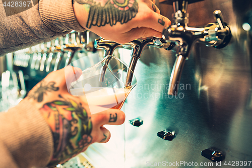 Image of Hand of bartender pouring a large lager beer in tap.