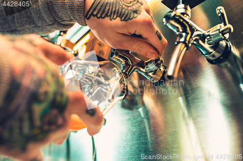 Image of Hand of bartender pouring a large lager beer in tap.