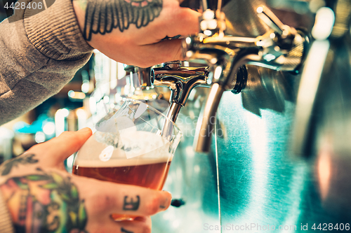 Image of Hand of bartender pouring a large lager beer in tap.