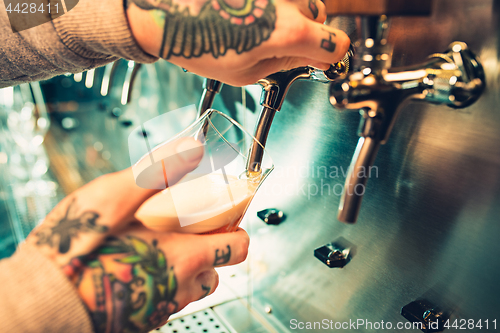 Image of Hand of bartender pouring a large lager beer in tap.