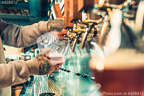 Image of Hand of bartender pouring a large lager beer in tap.