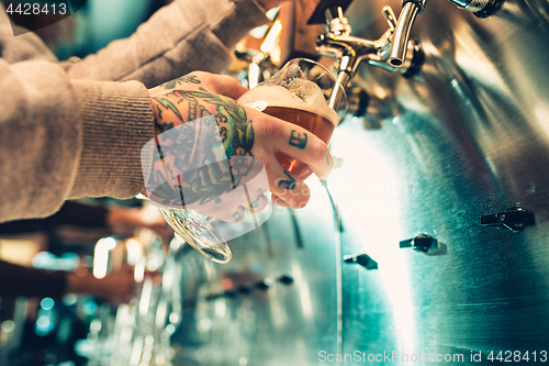 Image of Hand of bartender pouring a large lager beer in tap.