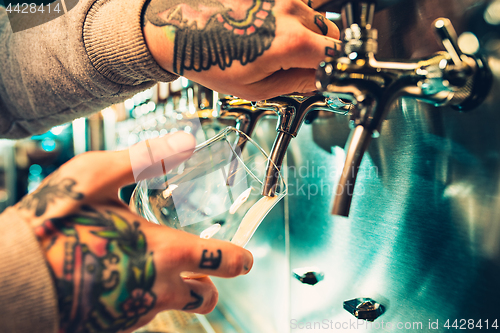 Image of Hand of bartender pouring a large lager beer in tap.