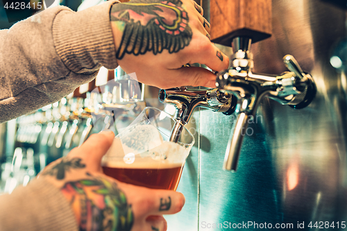 Image of Hand of bartender pouring a large lager beer in tap.