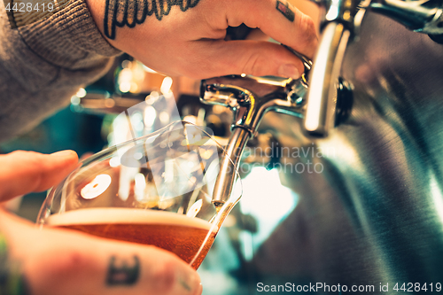 Image of Hand of bartender pouring a large lager beer in tap.