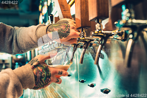 Image of Hand of bartender pouring a large lager beer in tap.