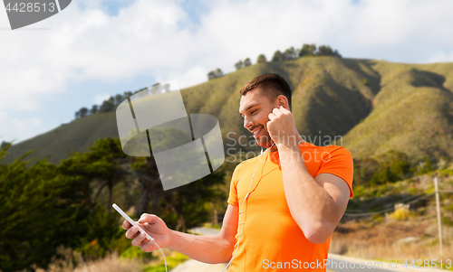 Image of man with smartphone and earphones over hills