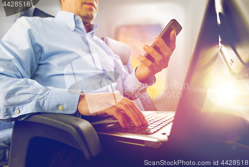 Image of businessman with smartphone and laptop in plane