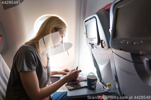 Image of Casual woman flying on commercial passengers airplane, filling in immigration form.