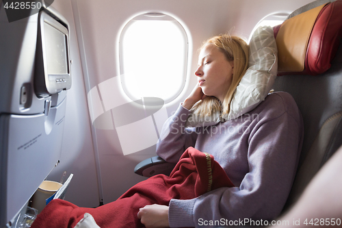 Image of Tired blonde casual caucasian lady sleepin on seat while traveling by airplane. Commercial transportation by planes.