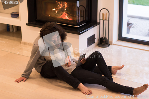 Image of multiethnic couple using tablet computer on the floor