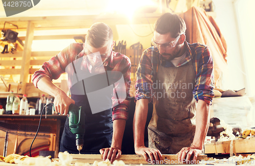 Image of carpenters with drill drilling plank at workshop