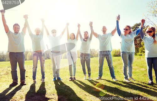 Image of group of happy volunteers holding hands outdoors