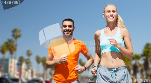 Image of smiling couple jogging at summer over venice beach