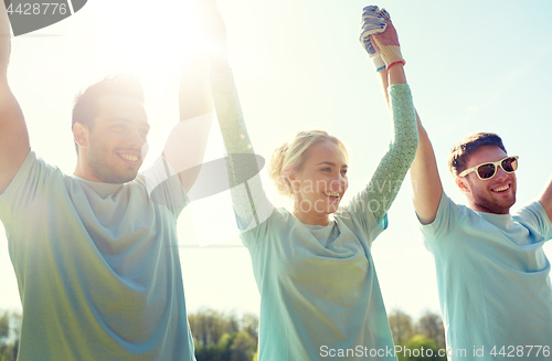 Image of group of happy volunteers holding hands outdoors