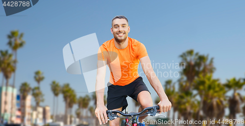 Image of happy young man riding bicycle over venice beach