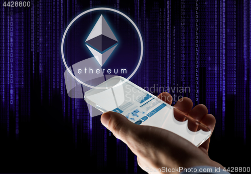 Image of hand with smartphone and ethereum hologram