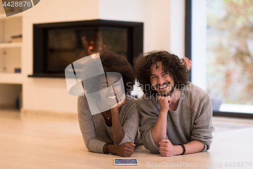 Image of multiethnic couple lying on the floor  in front of fireplace