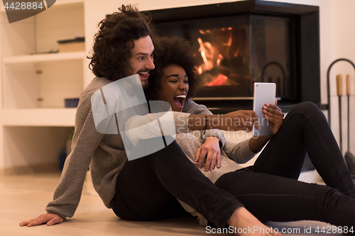 Image of multiethnic couple using tablet computer on the floor