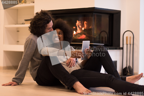 Image of multiethnic couple using tablet computer on the floor
