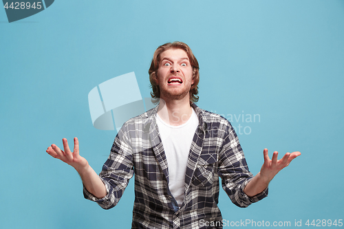 Image of The young emotional angry man screaming on blue studio background