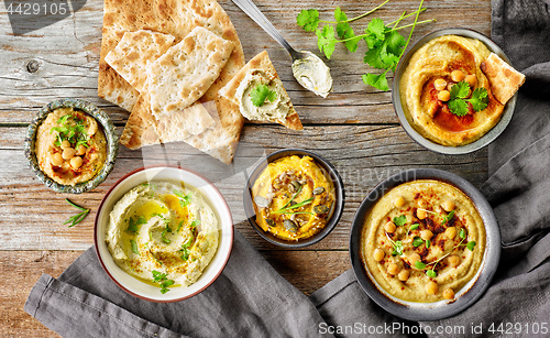 Image of various hummus spreads on wooden table