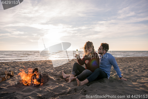 Image of Young Couple Sitting On The Beach beside Campfire drinking beer
