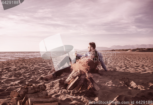 Image of Young Couple Sitting On The Beach beside Campfire drinking beer