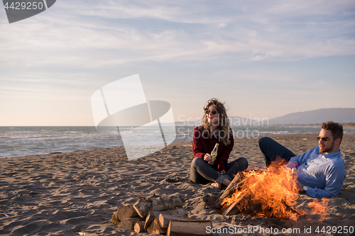 Image of Young Couple Sitting On The Beach beside Campfire drinking beer