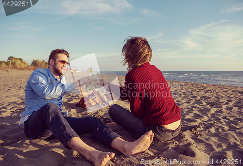 Image of Young Couple Sitting On The Beach beside Campfire drinking beer