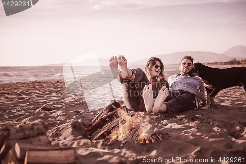 Image of Young Couple Sitting On The Beach beside Campfire drinking beer