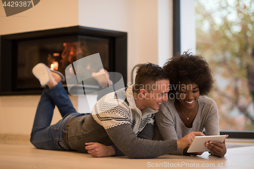 Image of multiethnic couple using tablet computer on the floor
