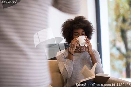 Image of black woman reading book  in front of fireplace