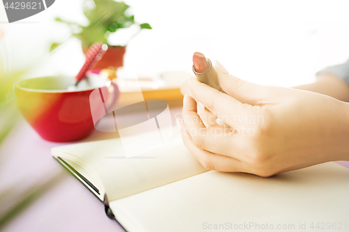 Image of The female hands holding pomade. The trendy pink desk.