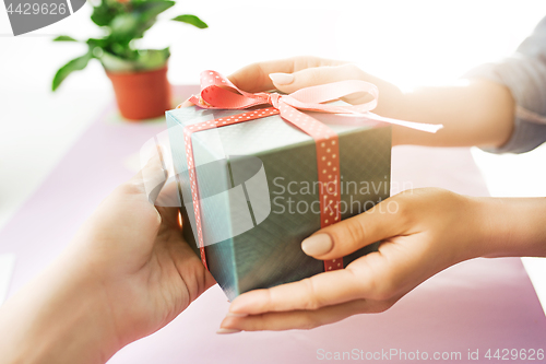 Image of Close-up of female hands holding a present. The trendy pink desk.