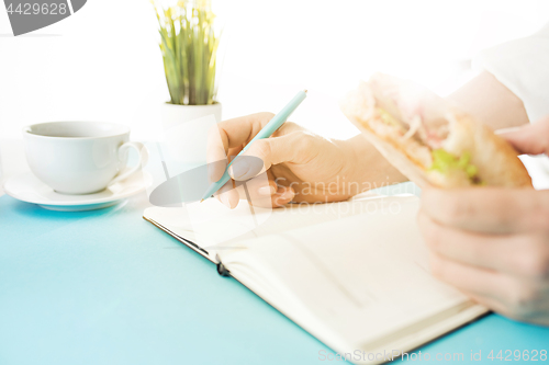 Image of The male hands holding pen and sandwich. The trendy blue desk.