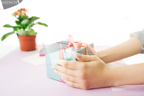 Image of Close-up of female hands holding a present. The trendy pink desk.