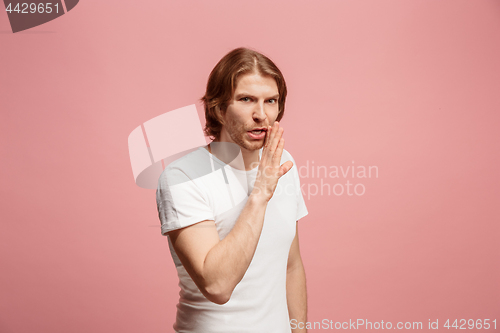 Image of The young man whispering a secret behind her hand over pink background