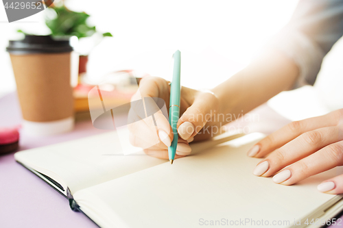 Image of The female hands holding pen. The trendy pink desk.