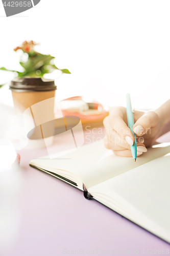 Image of The female hands holding pen. The trendy pink desk.