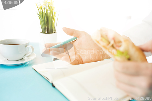 Image of The male hands holding pen and sandwich. The trendy blue desk.