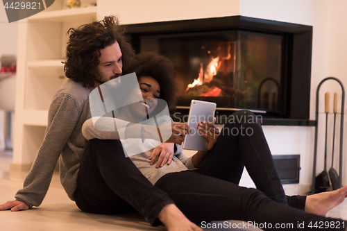 Image of multiethnic couple using tablet computer on the floor