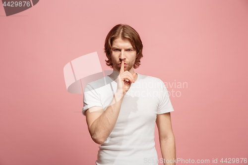 Image of The young man whispering a secret behind her hand over pink background