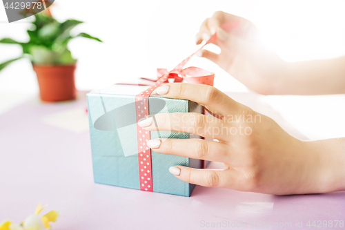 Image of Close-up of female hands holding a present. The trendy pink desk.