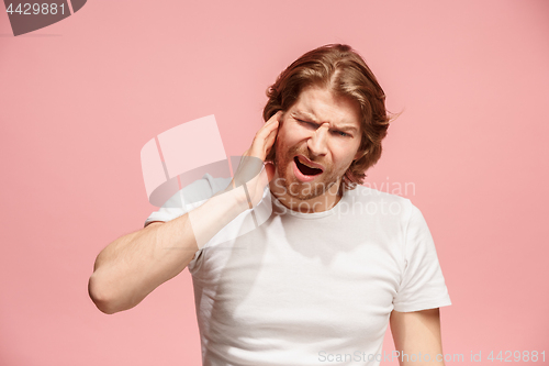 Image of The Ear ache. The sad man with headache or pain on a pink studio background.