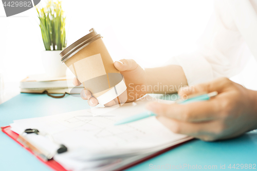 Image of The male hands holding pen and coffee. The trendy blue desk.